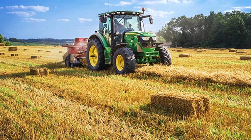 Farmer bailing hay on green tractor 