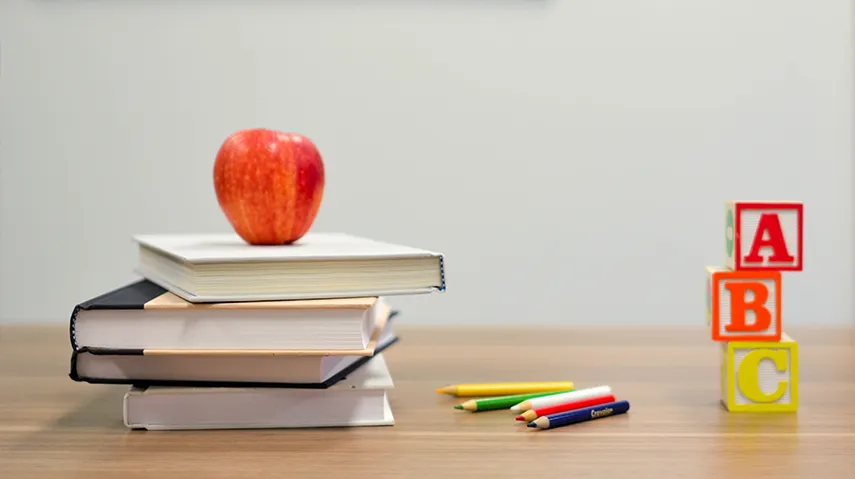 Red apple atop books next to school supplies