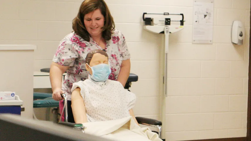 Student pushing a sim manikins in a wheelchair.